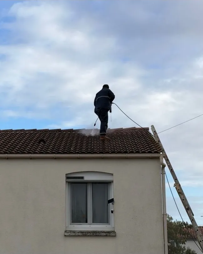 Jojakim Klein, de dos, sur le faîtage d'un toit de tuiles qu'il nettoie